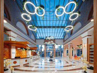 Ampia hall d'hotel con tetto in vetro, anelli luminosi circolari moderni e banchi di ricevimento.