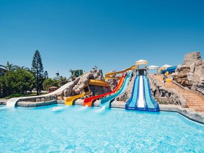 Più scivoli d'acqua conducono a una grande piscina dell'hotel sotto un cielo azzurro.