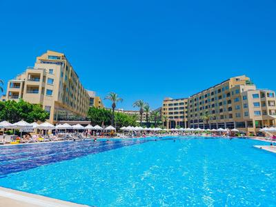 Grande piscina all'aperto davanti a due edifici alberghieri a più piani sotto un cielo azzurro limpido.