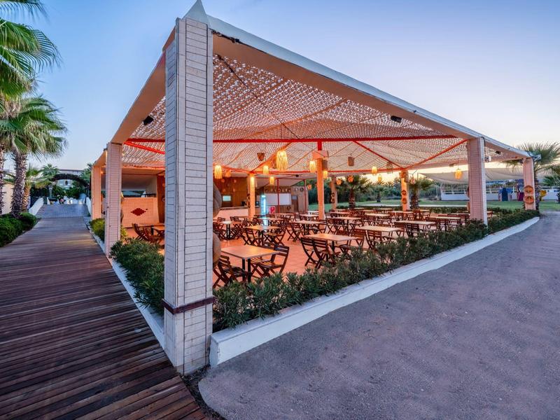 Padiglione aperto con tavoli e sedie in legno accanto a un pavimento in legno e un percorso al tramonto.