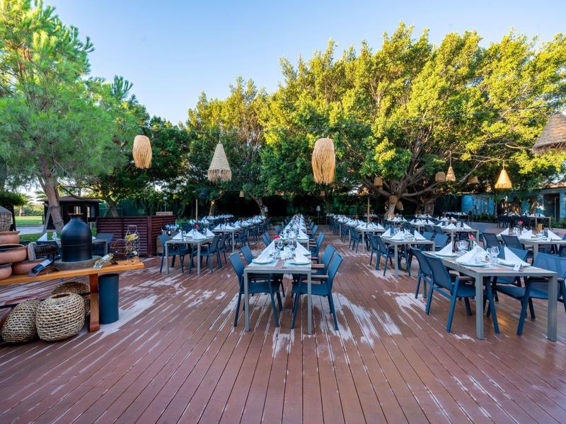 Area esterna del ristorante con tavoli e sedie su terrazza in legno circondata da alberi.