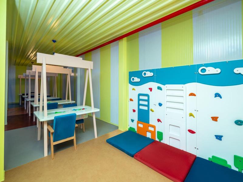 Sala giochi colorata con parete da arrampicata, materassini e sedie a dondolo per bambini.