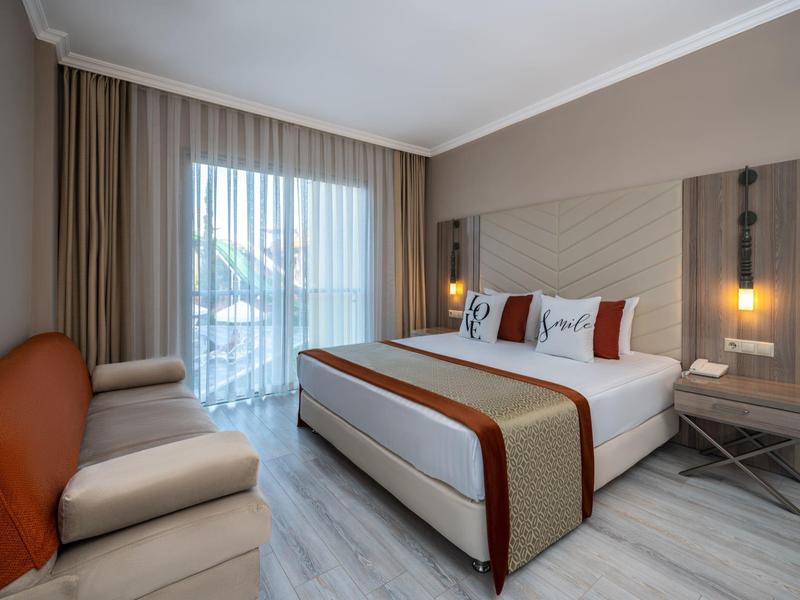 Camera d'hotel moderna con letto matrimoniale, divano e finestra a tutta altezza con tende.