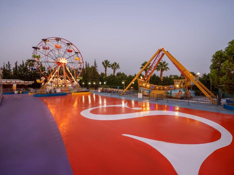 Parco divertimenti serale con ruota panoramica illuminata e carosello dietro a un sentiero colorato.