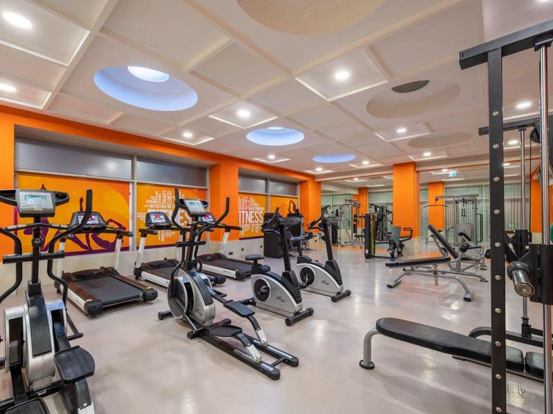 Palestra moderna con vari attrezzi da allenamento e pareti arancioni.