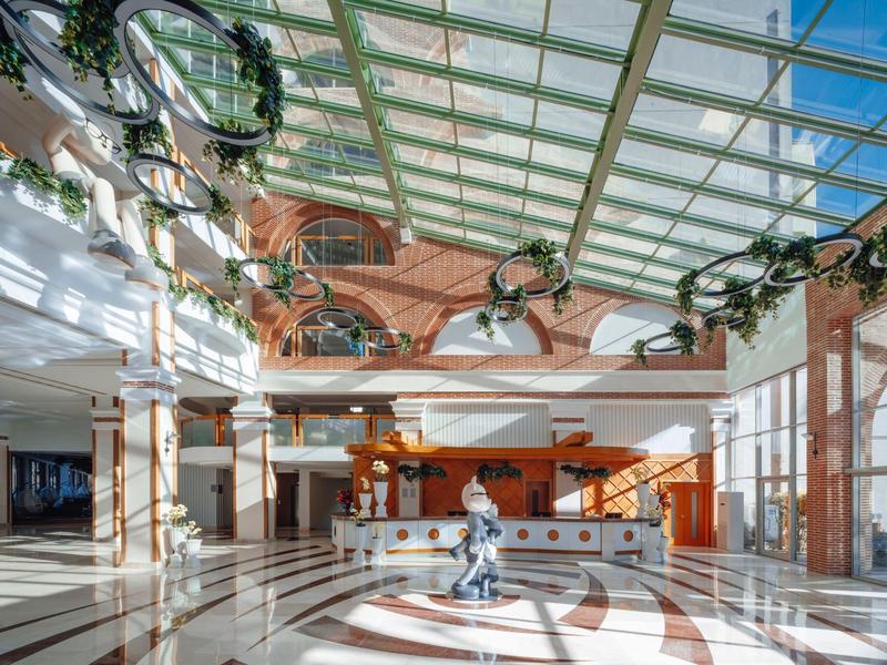 Ampia hall d'hotel con banco informazioni, soffitto in vetro e illuminazione moderna.