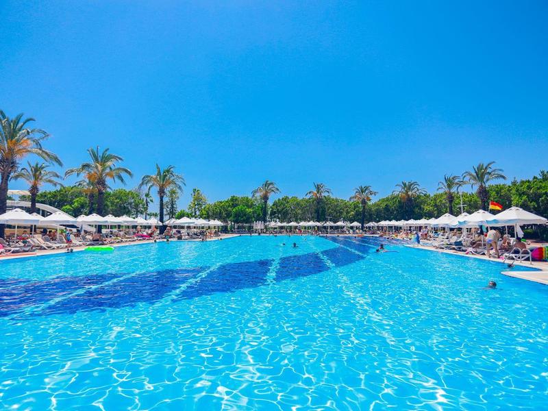 Grande piscina dell'hotel con acqua azzurra limpida e ombrelloni bianchi sotto un cielo soleggiato