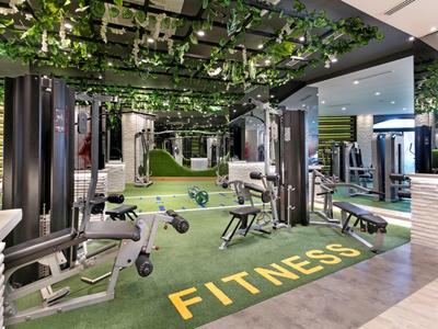 Moderner Fitnessraum mit Geräten, grünem Kunstgras und Decke mit hängenden Pflanzen.