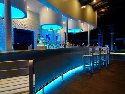 Area bar moderna in hotel con bancone illuminato di blu e sgabelli argentati di notte