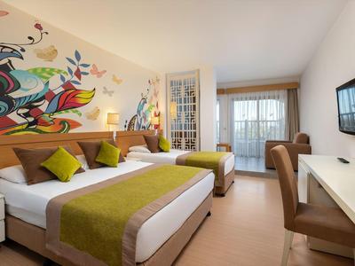 Camera d'hotel moderna con due letti, arte murale colorata e balcone con luce naturale.
