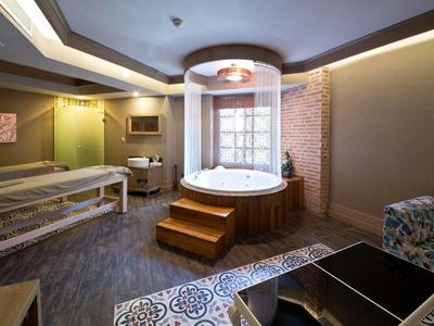 Sala benessere moderna con vasca idromassaggio, lettino da massaggio e zona salotto accogliente.