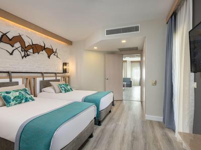 Camera d'hotel moderna con due letti, accenti turchesi e pavimento in legno.