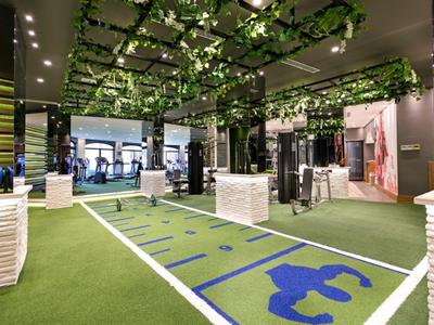 Modernes Fitnessstudio mit grünen Dekorationen und Sportgeräten auf Kunstrasenboden