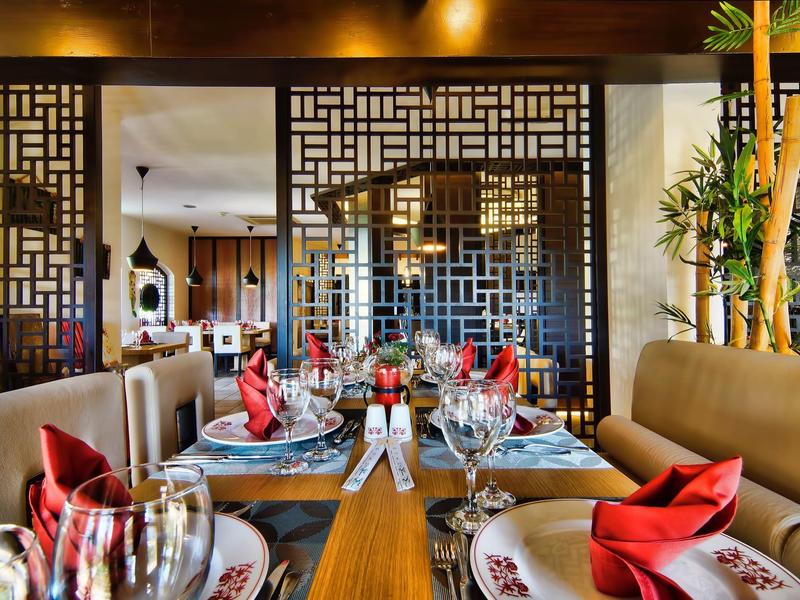 Ristorante elegante con decorazioni asiatiche, tavolo apparecchiato con tovaglioli rossi, atmosfera accogliente.