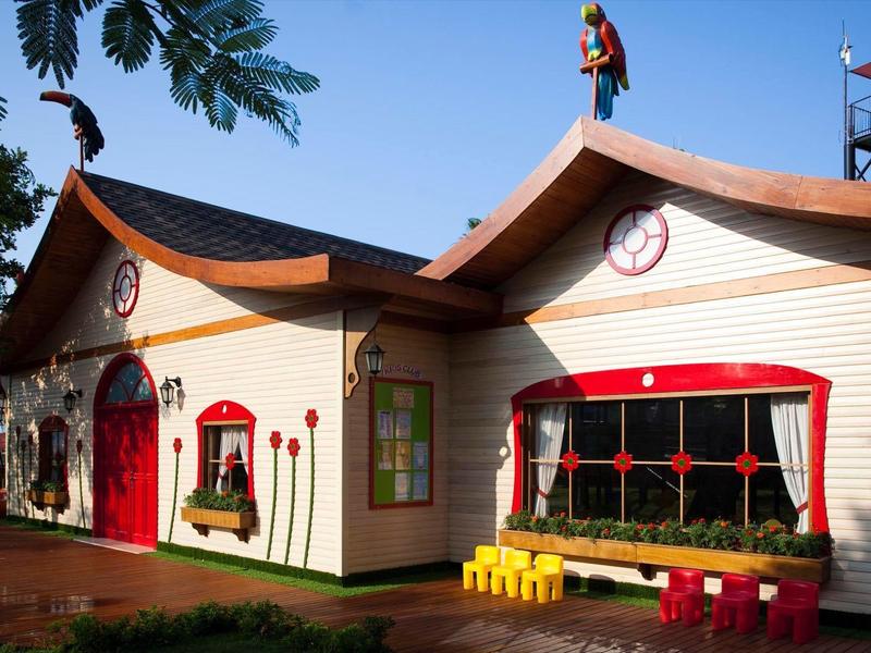 Casa colorata con orologi, panchine gialle e cielo blu sullo sfondo.