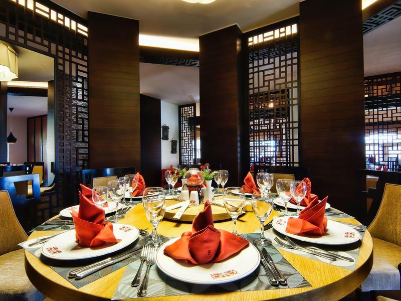 Ristorante elegante con tavolo rotondo apparecchiato con piatti bianchi, tovaglioli rossi e posate.