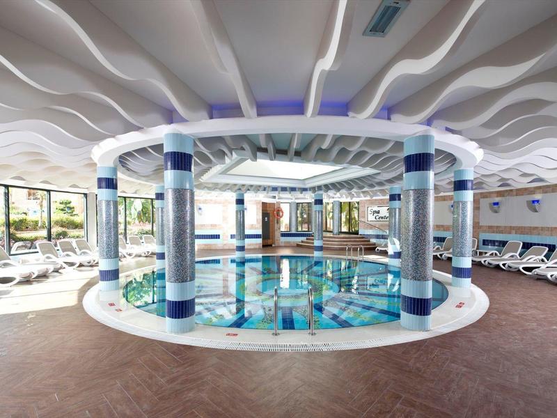 Piscina coperta moderna con colonne decorative e lettini ai lati.