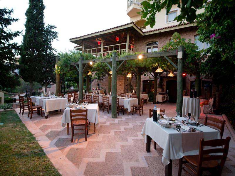 Accogliente area esterna con tavoli coperti e sedie sotto gli alberi vicino a un edificio.