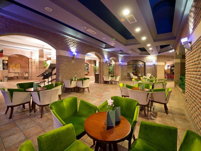 Elegante area lounge dell'hotel con poltrone verdi e tavoli in ambiente illuminato caldamente.