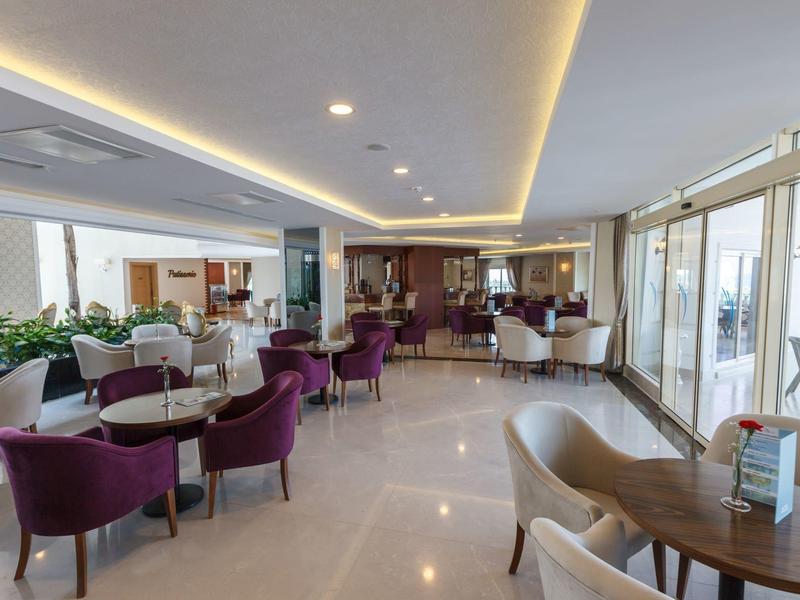 Lounge dell'hotel moderna e luminosa con poltrone viola e beige e grandi finestre