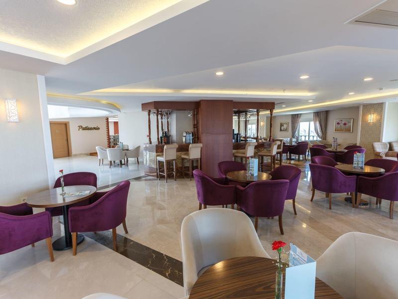 Ristorante dell'hotel luminoso con sedie viola, tavoli in legno e illuminazione a soffitto moderna.