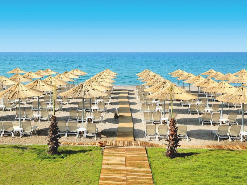 Lettini e ombrelloni disposti simmetricamente sulla spiaggia con vista sul mare.