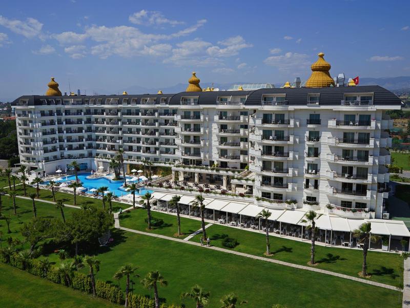 Grande hotel su più piani con piscine e giardini ben curati in una giornata di sole.