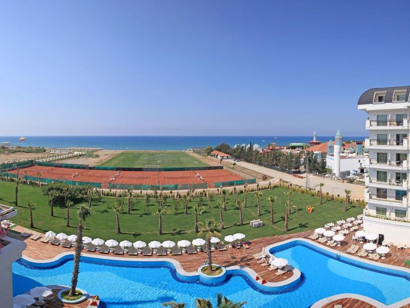 Vista di una piscina dell'hotel, pista di atletica e mare sullo sfondo con cielo sereno.