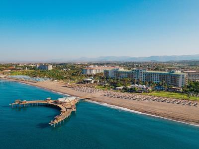 Spiaggia con resort alberghieri, lettini e una passerella di legno che si estende nel mare sotto un cielo limpido.