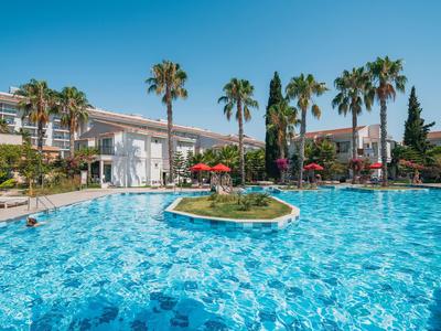 Grande piscina dell'hotel con palme e ombrelloni sotto un cielo azzurro.