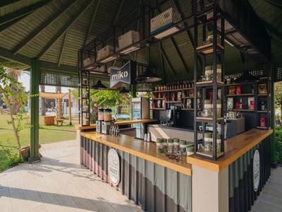 Area bar moderna con bancone in legno e sgabelli in un padiglione aperto circondato dal verde.