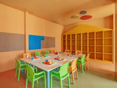 Stanza colorata dell'asilo con tavoli, sedie e scaffali per giocattoli e materiali.