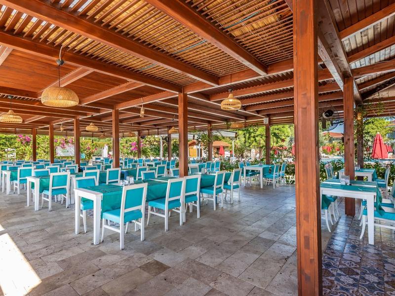 Ampia area esterna coperta di un hotel con sedie blu e tavoli bianchi.