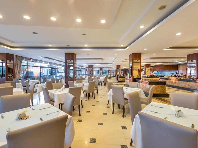 Ristorante moderno e luminoso con tavoli bianchi, sedie beige, ampia area buffet e illuminazione soffusa.
