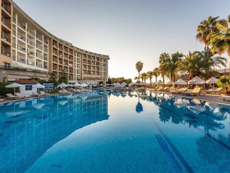 Grande piscina dell'hotel con lettini e palme al tramonto