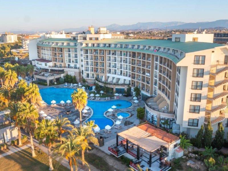 Hotel moderno con grande piscina e palme in posizione soleggiata.