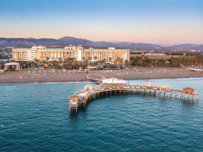 Grande hotel sulla spiaggia con un lungo molo che si estende nel mare al tramonto.