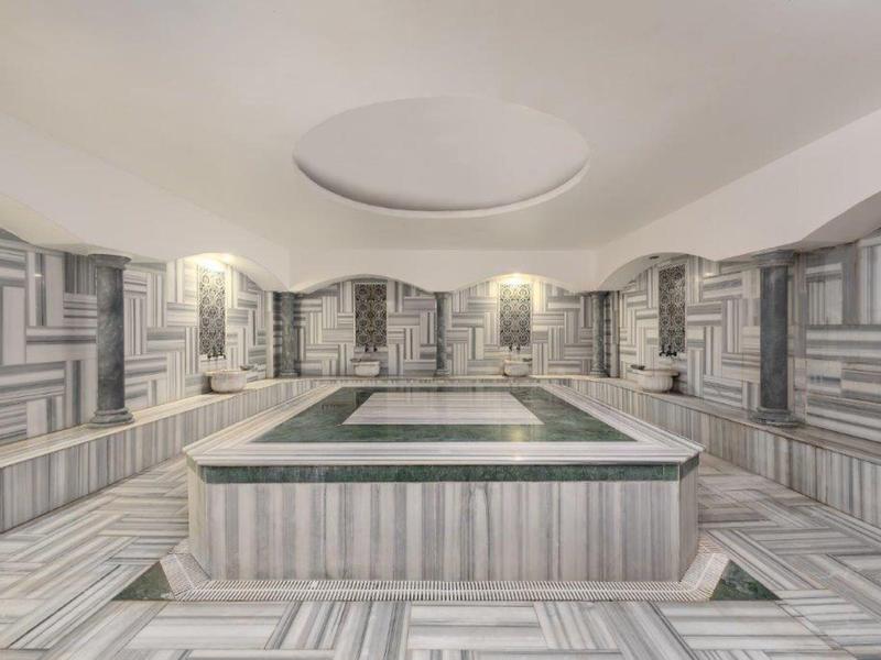 Area benessere moderna con vasca idromassaggio rettangolare e pareti decorate con motivi geometrici.