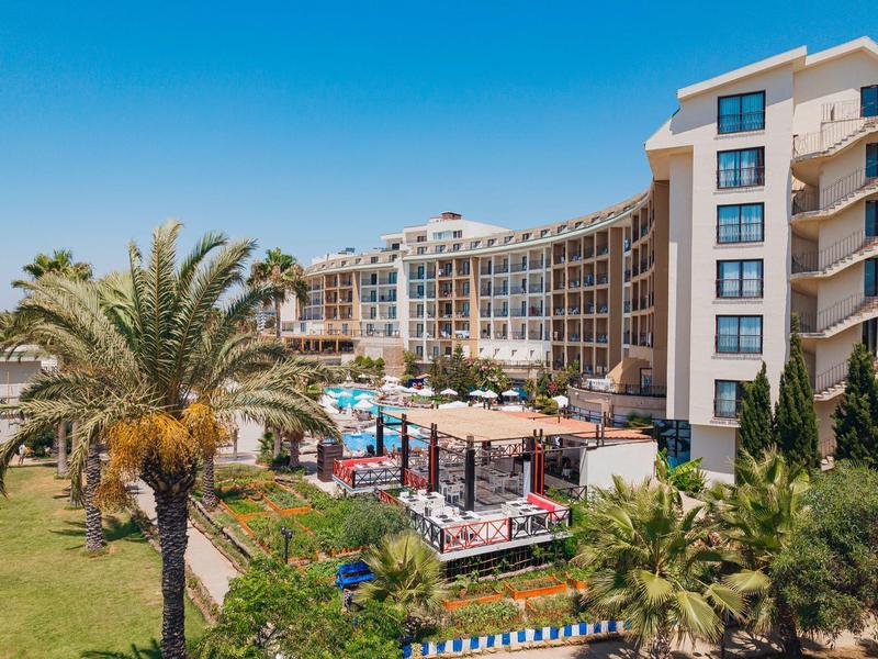 Grande edificio dell'hotel su più piani circondato da palme sotto un cielo azzurro.
