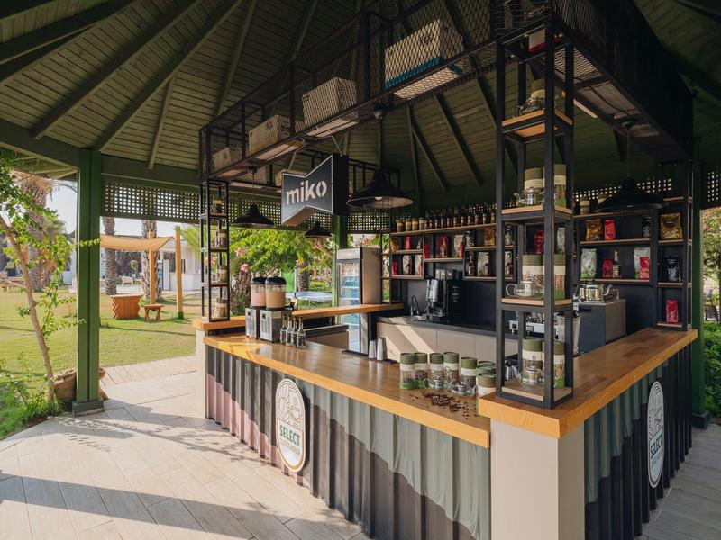 Area bar moderna con bancone in legno e sgabelli in un padiglione aperto circondato dal verde.