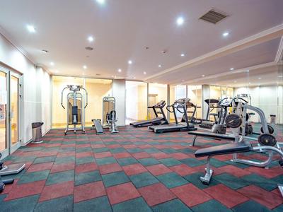 Heller Fitnessraum mit buntem gepolstertem Boden, Trainingsgeräten und Spiegelwand.