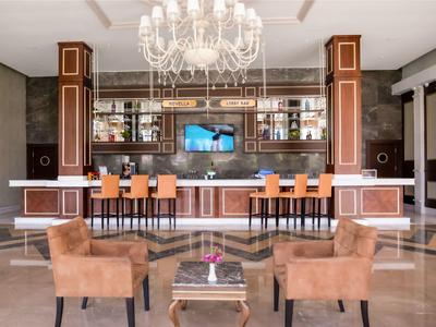 Elegante Bar mit braunen Sesseln, orangefarbenen Barhockern und großem Kronleuchter.
