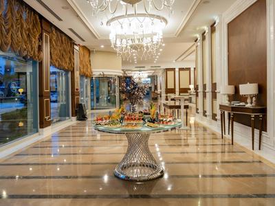 Großer, heller Hotellobby mit Kronleuchtern, Marmorboden und mittig platziertem Blumengesteck.