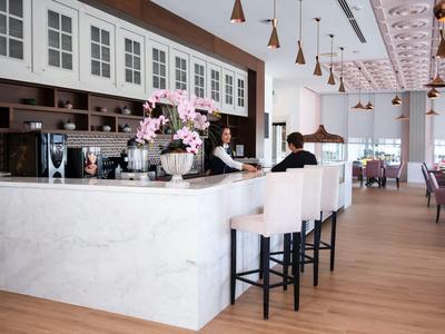 Moderner Cafébereich mit Marmorbar, weißen Barhockern, Holzboden und Deckenlampen.