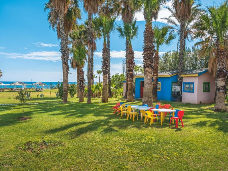 Tavoli e sedie colorati su un prato vicino a palme con vista sul mare.