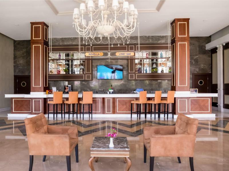 Elegante bar dell'hotel con lampadario di cristallo, poltrone marroni e sgabelli arancioni.