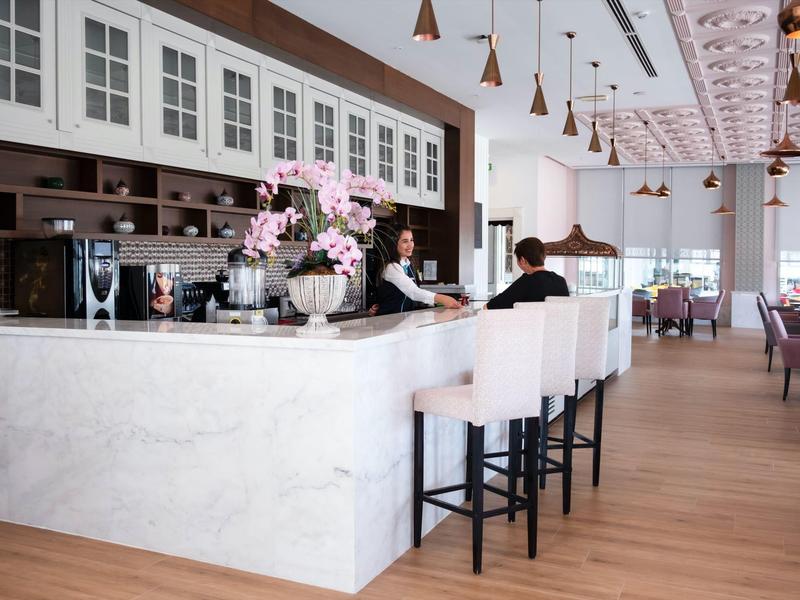 Bar dell'hotel moderno con sgabelli bianchi, piano in marmo e fiori decorativi.