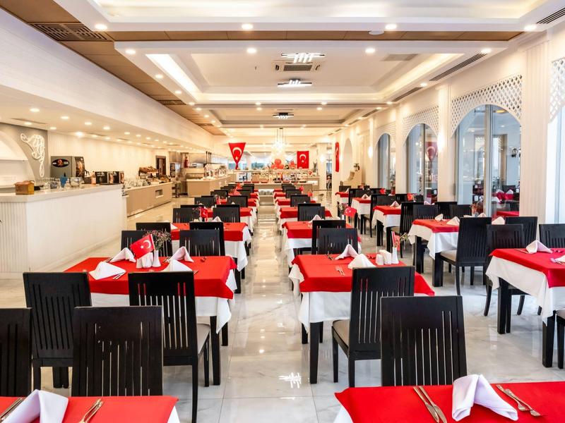 Ampia sala da pranzo ben illuminata con tavoli apparecchiati di rosso e sedie nere.
