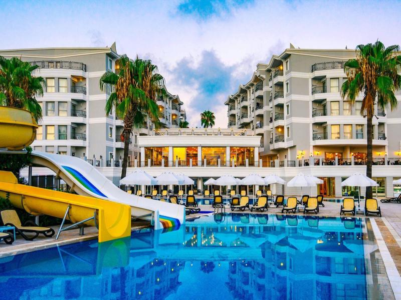 Hotel con piscina, scivoli d'acqua e lettini sotto un cielo azzurro.