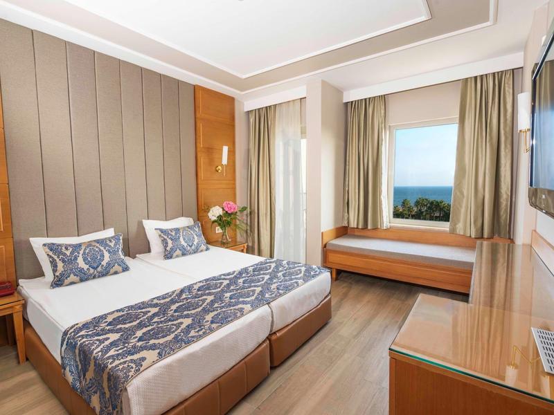 Camera d'hotel luminosa con due letti singoli, seduta finestra e vista mare.